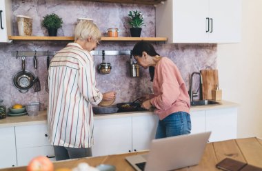 Asyalı kız arkadaş mutfakta birlikte yemek pişirirken, Asyalı bir kadının kasedeki malzemeleri karıştırması yan görünüm.