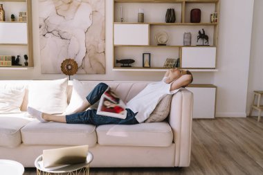 Modern oturma odasında tek başına dinlenirken rahat bir kanepede uyuyan, gündelik giysiler giymiş olgun bir kadın.