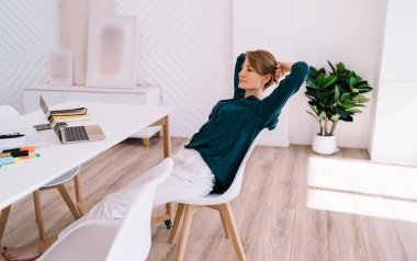 Evde işi bitirdikten sonra elleri başının arkasında oturan ve netbook ekranına bakan olgun kadın serbest stilistin yan görüntüsü