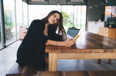 Siyah elbiseli İspanyol kadının laptopun yanında oturması ve akıllı telefonlara bakarken gözlerini kaçırması.