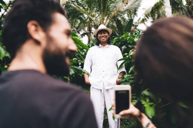 Bali 'de başarılı bir proje üzerinde çalışırken Endonezyalı gülümseyen erkek kahve çiftçisinin cep telefonuyla fotoğraflarını çeken çok ırklı mutlu girişimciler.