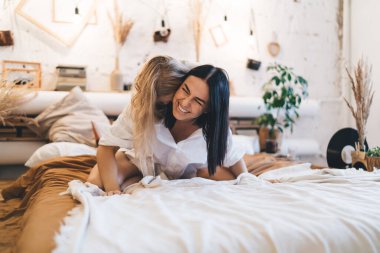 Beyaz gömlekli komik sarışın kız yatak odasında dinlenirken ve yatakta birlikte oynarken gülüyor.