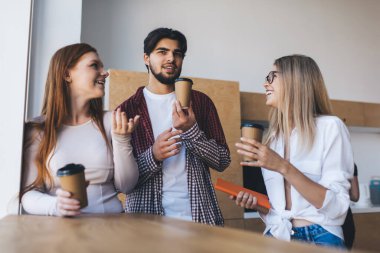 Gündelik giysiler içinde bir grup genç iş arkadaşı kahve fincanlarıyla masada duruyor ve modern ofiste boş zamanlarını iş projelerinden bahsederek geçiriyorlar.