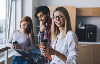 Ofis mutfağında netbook ile beyin fırtınası yaparken ve başarılı bir proje üzerinde çalışırken gündelik giysiler içinde, bir fincan kahve içerek gülümseyen çok ırklı meslektaşlar.