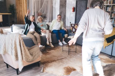 Bir grup yaşlı insan kanepede dinleniyor ve hafta sonunu rahat bir oturma odasında birlikte geçiriyorlar. Bu arada ön planda isimsiz bir kadının dansına tezahürat ediyorlar.