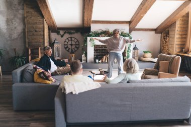 Kanepede oturan son sınıf öğrencilerinin ve olgun bir kadının boş zamanlarında evde oturup eğlenmesi.