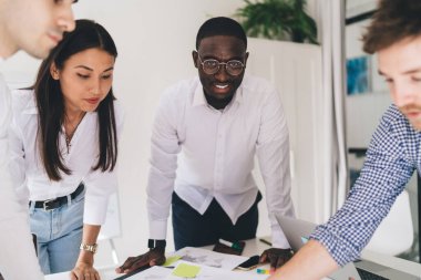 Bir grup güler yüzlü, çok kültürlü iş adamı konferans odasında durup başarılı bir başlangıç projesi üzerinde çalışırken beyin fırtınası yapıyor ve fikir paylaşıyorlar.