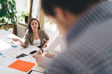Gülümseyen ve dizüstü bilgisayara bakan neşeli genç bir kadın masada kağıtlarla oturuyor ve ofisteki bulanık erkek sunucunun oturumuna katılıyor.