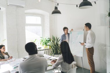 Modern yönetim kurulunda toplanan çok ırklı meslektaşların camdan duvarına bakın. Erkek hoparlörler ise projenin sunumunu yapıyor.