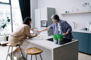 Kızının bar taburesinde oturup, planlayıcıyı yaşlı anneye göstermesi, çağdaş mutfakta zaman geçirirken planlarını tartışması.