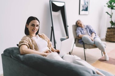 Dizüstü bilgisayarda yazan olumlu bir kadın yeni bilgiler öğreniyor. Aynanın yanındaki koltukta oturuyor. Yaşlı anne de koltukta dinleniyor.