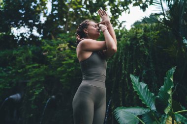 Spor kıyafetleri içinde düşük açılı sakin bir kadın. Gözleri kapalı. Pranayama nefes egzersizleri yapıyor.