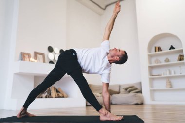 Evde Utthita Trikonasana egzersizi yaparken yoga sırasında minder üzerinde duran yalınayak esnek erkek sporcunun alçak açısı