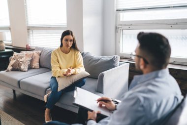 Erkek psikolog, modern klinikte birbirlerine açıklarken ve bakarken endişeli genç kadın hastaların pano sağlık sorunlarına not alıyor.