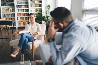 Modern ofiste rahat bir koltukta otururken psikoterapistle sorunlardan bahseden üzgün erkek müşterinin yan görüntüsü