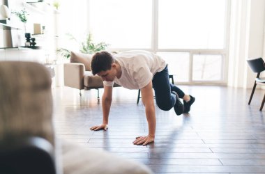 Aktif giyimli erkek sporcu. Kereste pozisyonu alıyor. Sabahları kolları üzerinde duruyor ve tek bacağı çalıştırıyor.