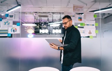 Ofiste buluşmadan önce sunum slaytlarını kontrol edip analiz ederken ekrana bakan konsantre sakallı erkek girişimcinin kenar görüntüsü