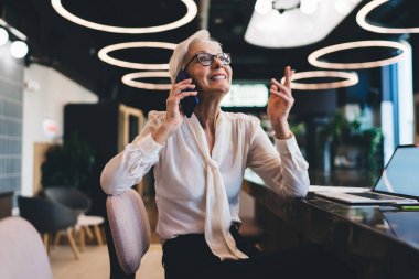 Ofiste boş zamanlarında gözlüklü, dizüstü bilgisayarı olan ve gözlerini kaçıran yaşlı, pozitif girişimci bir kadın.