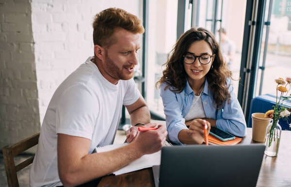Содержание женщины и мужчины в повседневной одежде, глядя на экран ноутбука и принимая новый бизнес-проект, сидя вместе за столом кафе