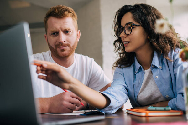 Сосредоточенные мужчина и женщина в повседневной одежде рассматривая информацию о бизнес-проекте и глядя на экран нетбука, сидя вместе в кафе во время перерыва