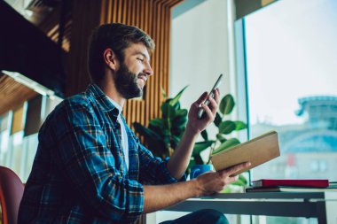 Mutlu sakallı erkek işçinin cep telefonundan mesaj almasına ek olarak modern ofis günlerinde defter ve defter okurken cep telefonuna mesaj gelmesi.