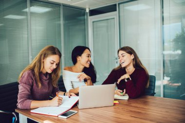 Modern işyerlerinde başarılı bir proje üzerinde çalışırken bilgisayarlı çok ırklı iş arkadaşları beyin fırtınası yaparken organizatörden notlar alan mutlu kadın ofis çalışanı.
