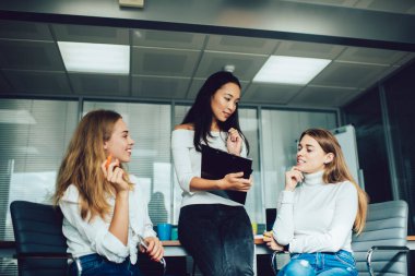 Akıllı telefon ve not panosuyla güncel iş yerinde buluşurken yeni iş stratejilerini tartışan çok ırklı genç kadınların düşük açısı