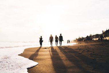 Tanımlanamayan bir grup insanın tüm vücudu kumlu sahilde geziniyor ve yaz tatilinde bulutlu günbatımı gökyüzünün keyfini çıkarıyor.