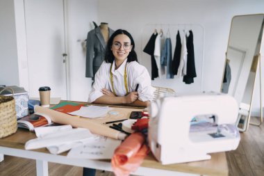 Profesyonel dikiş atölyesinde kıyafet tasarımı yaparken rahat gömlekli, yüksek açılı kadın terzi.
