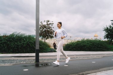 Yağmurlu bir günde şehir sokaklarında asfalt yolda koşarken gülümseyen ve ileriye bakan sporcu kadın sporcuların yan görüntüsü