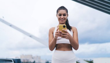 Büyük şehirde kulaklıkların içinde dururken cep telefonu cihazında cep telefonu mesajı okuyan çekici bir kadın. Akıllı telefon uygulaması ile kulaklıkla müzik dinleyen genç bir kadın. Taşınabilir internet