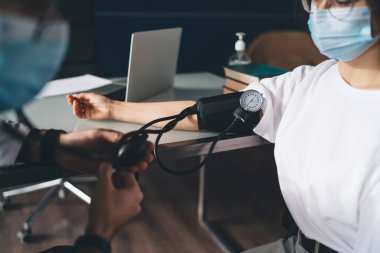 Hastanedeki konsültasyon sırasında hasta sağlığını kontrol etmek için tonometre kullanırken yüz maskesi takan isimsiz bir erkek ve kadın.