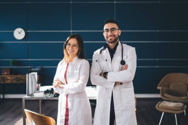 Gözlüklü neşeli kadın ve erkek doktorlar modern klinikte çalışırken masanın yanında el ele tutuşup duruyorlar.
