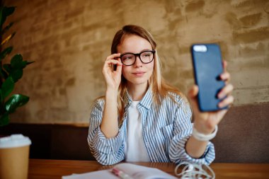 Cep telefonuyla kendi portresini çekerken gülümseyen serbest çalışan bir kadın ve kahve dükkanında çalışmaktan ürperen bir kadın.