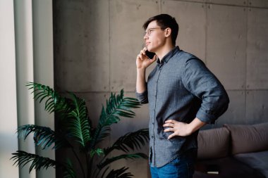 Günlük kıyafet ve gözlük takmış bir erkek girişimcinin teneffüs sırasında tuvalette telefon görüşmesi yaparken görüntüsü.