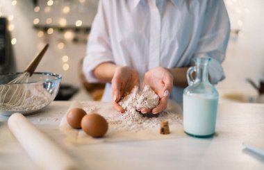 Beyaz ahşap masada hamuru tatlıya hazırlarken unlu yumurtalarla yemek pişiren tanınmamış bir kadın.