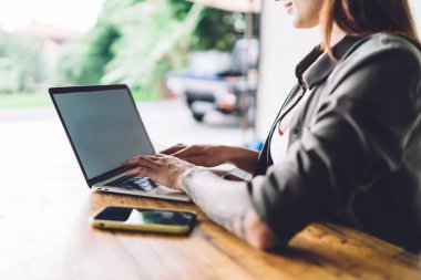 Tanımlanamayan, kolunda dövmesi olan, ahşap bir masada oturan, netbook 'ta yazan ve kafedeki iş projesinde uzaktan çalışan kadın serbest yazar.