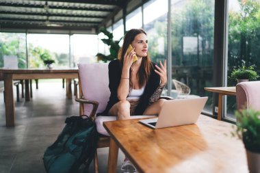 Günlük giysiler içinde genç bir kadın dizüstü bilgisayarla tahta masada oturuyor ve uzaktan kumandalı bir projede çalışırken gözlerini kaçırıyor.