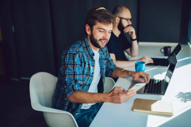 Akıllı telefonlu ve bilgisayarlı akıllı serbest çalışan sakallı bir erkek ofisteki erkek arkadaşının yanında oturuyor.