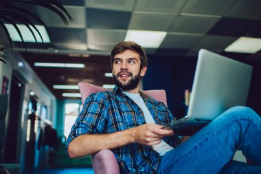 Modern ofiste dizüstü bilgisayarla çalışırken şık giyinen, düşük açılı, serbest çalışan genç bir erkek.