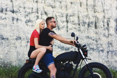 Moda kıyafetleri giymiş, hafta sonları motosiklet süren, sevgilisiyle motosiklete binen ve reklam alanının yakınına taşınan yakışıklı bir çift.