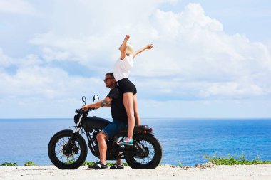 Güzel deniz manzaralı mutlu genç kadın sahilde gezen yakışıklı erkek arkadaşla romantik balayının keyfini çıkarıyor motosiklet süren aşıklar özgürce vakit geçiriyorlar.