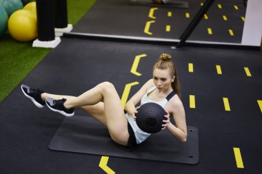 Beden eğitimi sırasında spor minderinde bacaklarınızı esneterek ve topu bir taraftan diğer tarafa hareket ettirerek diğer tarafa bakan formda bayan sporcu.