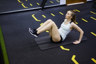 Zemini destekleyen elleri ve bacaklarını havaya kaldıran ve spor salonunda kriç egzersizi yapan formda bir bayan sporcunun bakışları yukarıdan başka yöne bakıyor.