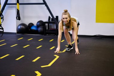 Genç, zayıf, sarı saçlı spor elbiseli bir kadın. Modern spor salonunda sarı çizgiler ve eğitim ekipmanlarıyla egzersiz yapıyorlar.