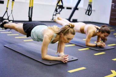 Çağdaş spor salonunda yoğun egzersiz sırasında karın kaslarını TRX kayışlarıyla çalıştırırken spor yapan konsantre bayan sporcular