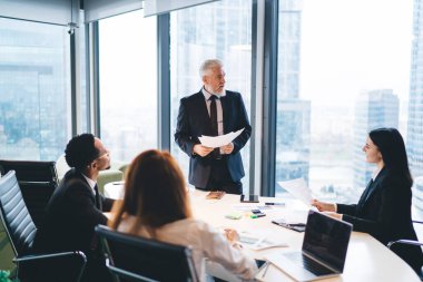 Bir grup çok ırklı iş arkadaşı masada otururken orta yaşlı profesyonel, toplantı sırasında projeyi müdüre anlatıyor.