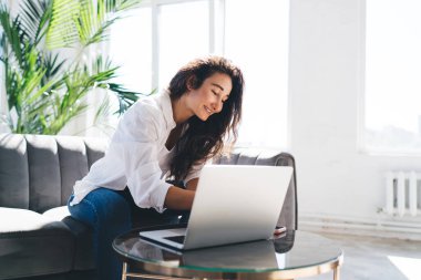 Genç İspanyol bayan girişimci kanepede dinleniyor ve evde boş zamanlarının keyfini çıkarırken bilgisayarlı akıllı telefon ekranına bakıyor.