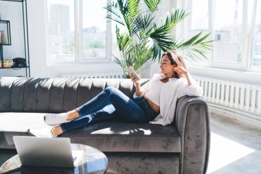 Boş zamanlarında genç İspanyol kadın cep telefonunun ekranına bakarken ve kanepede dinlenirken yan görüntüsü