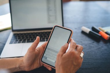 Tahta masada dizüstü bilgisayarla uzaktan çalışan ve iş yerinde sohbet ederken akıllı telefon tutan isimsiz bir serbest yazar.